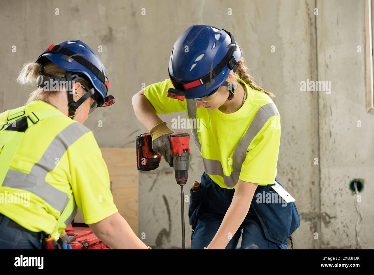 Female engineer using drill while working with coworker at construction site Stock Photo