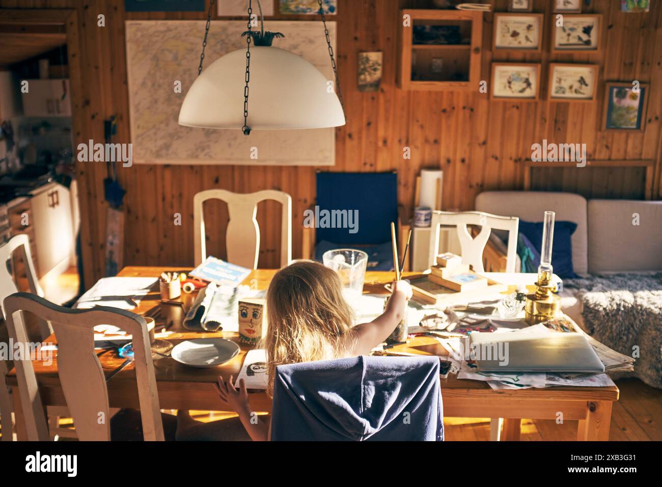 Rear view of girl painting while sitting at dining table in living room Stock Photo