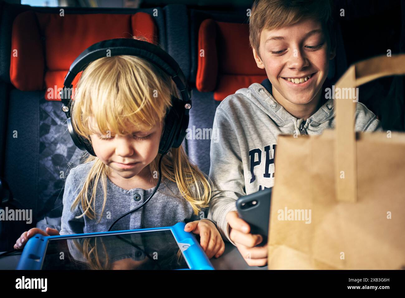 Smiling boy sitting by sister using digital tablet in train Stock Photo