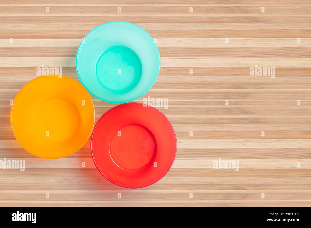 Three different colored plastic empty bowl on wooden table. Top view Stock Photo