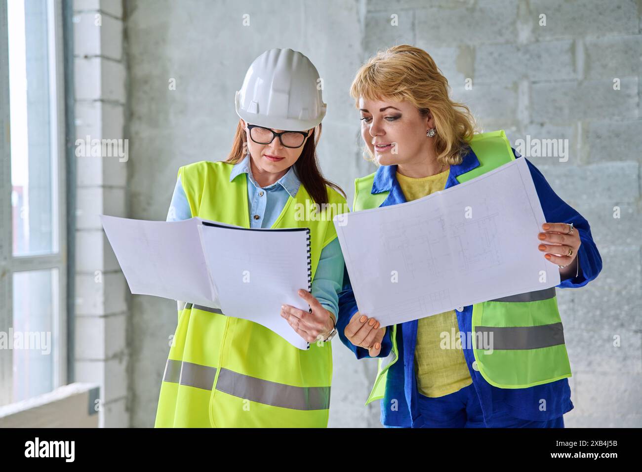 Two female industrial workers with technical plan at construction site Stock Photo