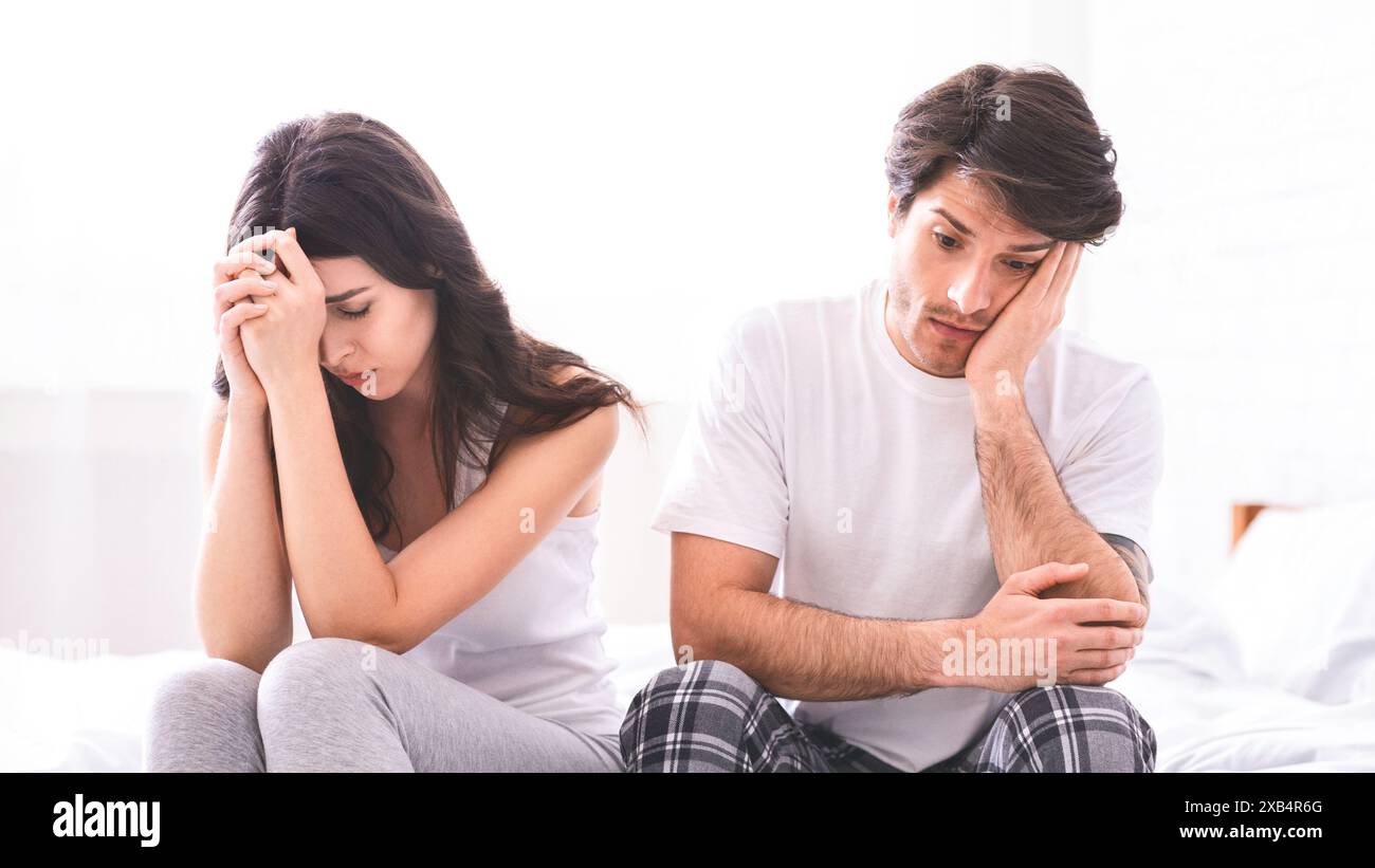 Couple Sitting on Bed With Sad Expressions Stock Photo