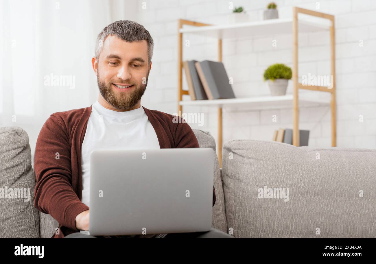 Cheerful Man Sitting on Couch Using Laptop Stock Photo