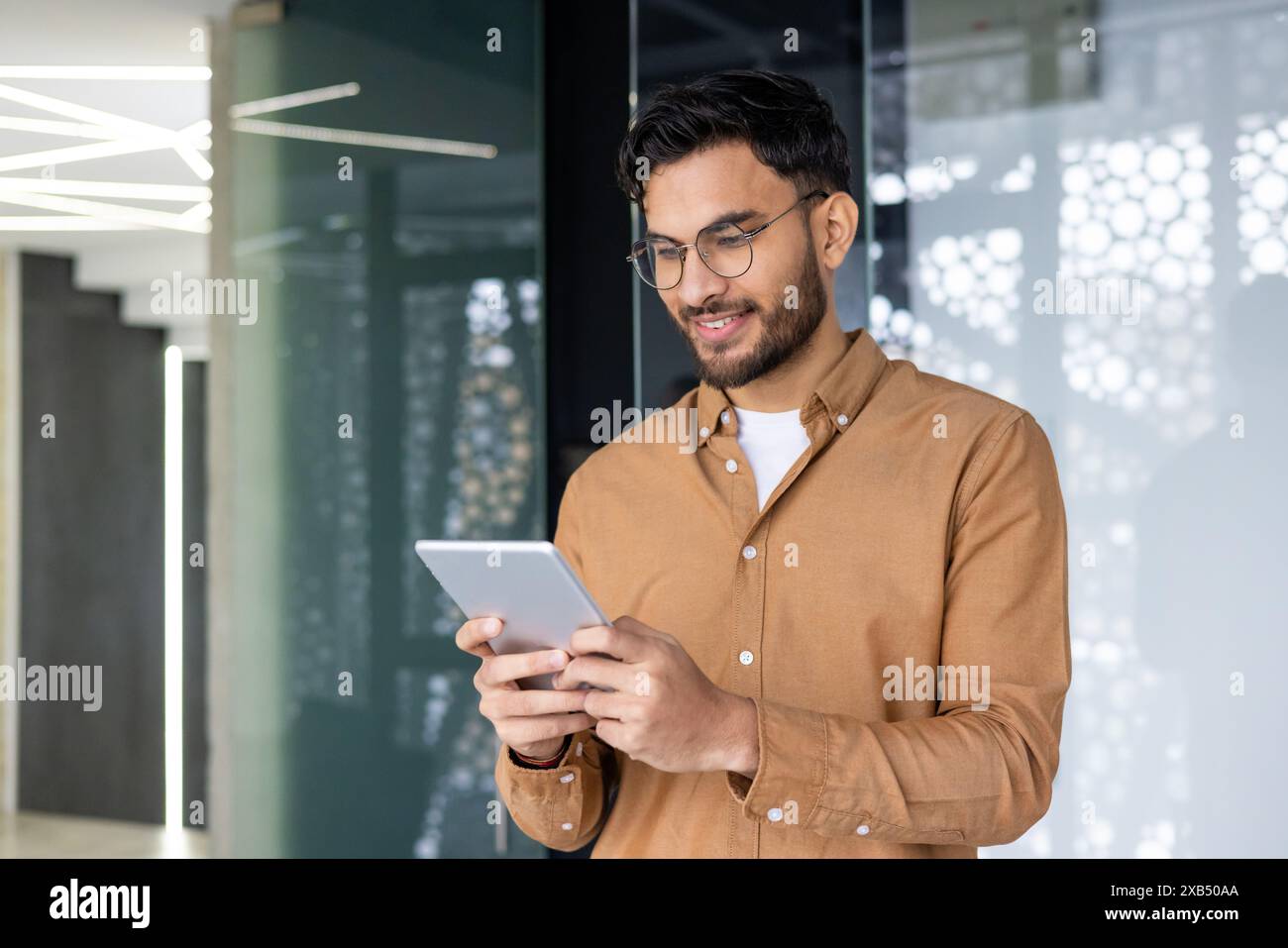 Young smiling Muslim male programmer and designer standing in modern office and using tablet. Stock Photo