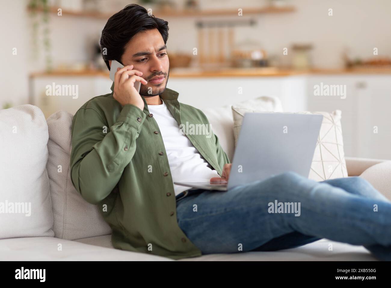 Man Talking On Phone While Working On Laptop From Home Stock Photo