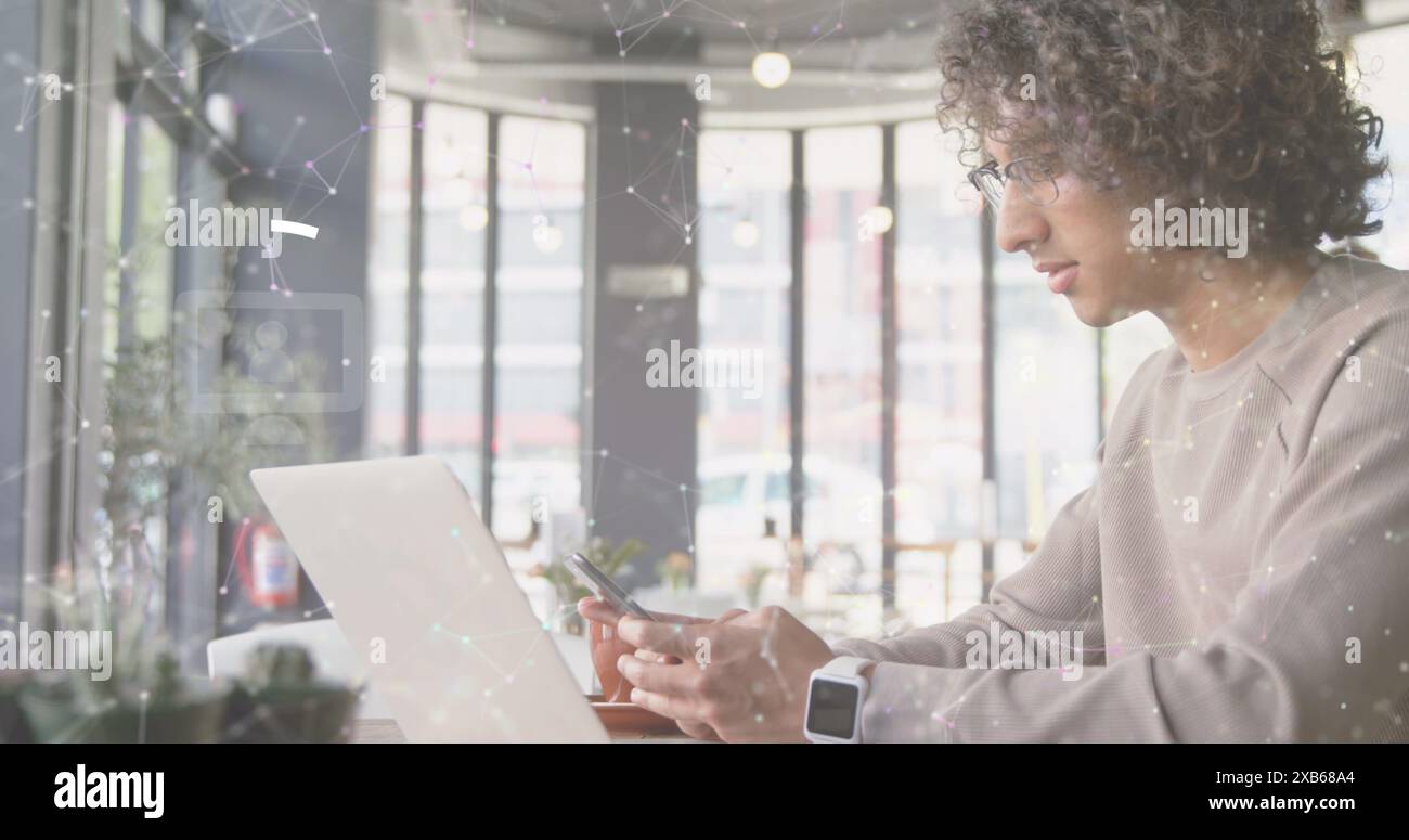 Young biracial man using smartphone while working on laptop in modern cafe Stock Photo