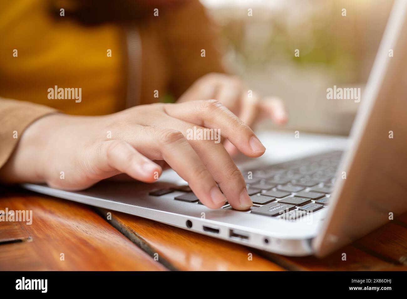 A close-up image of a woman working remotely from a cafe, working on her laptop computer, typing on the laptop keyboard, responding to emails or surfi Stock Photo