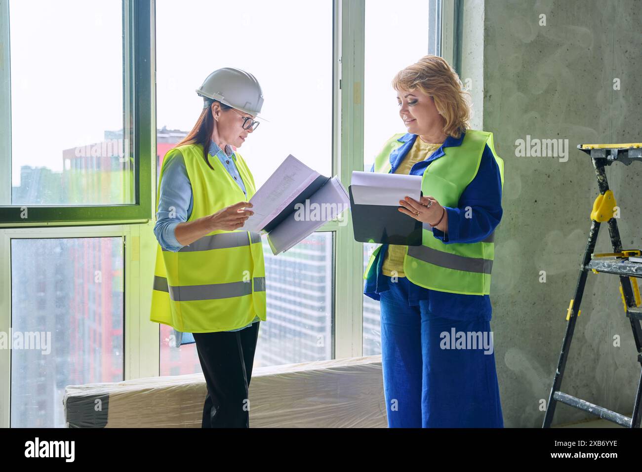 Two female industrial workers with technical plan at construction site Stock Photo