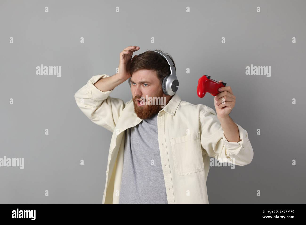 Confused man in headphones with game controller on grey background ...