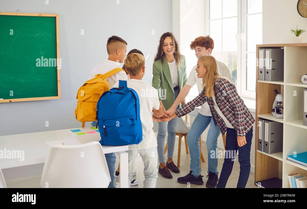 Happy school children with teacher standing in the classroom putting ...