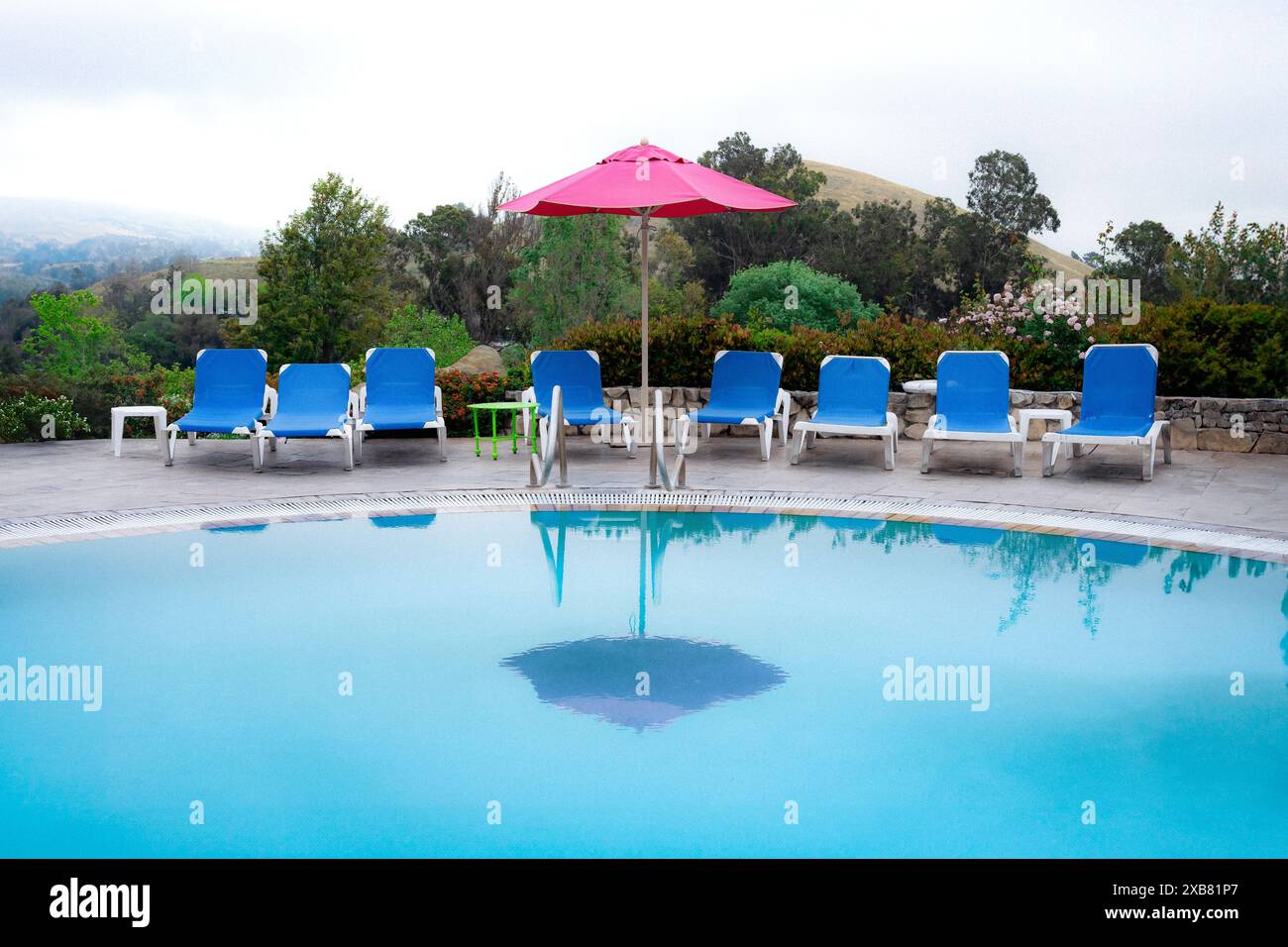 A swimming pool with a red umbrella and lounge chairs Stock Photo - Alamy
