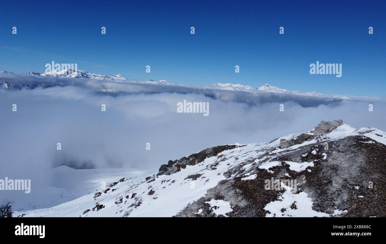 A partially snow-covered mountain peak above clouds Stock Photo