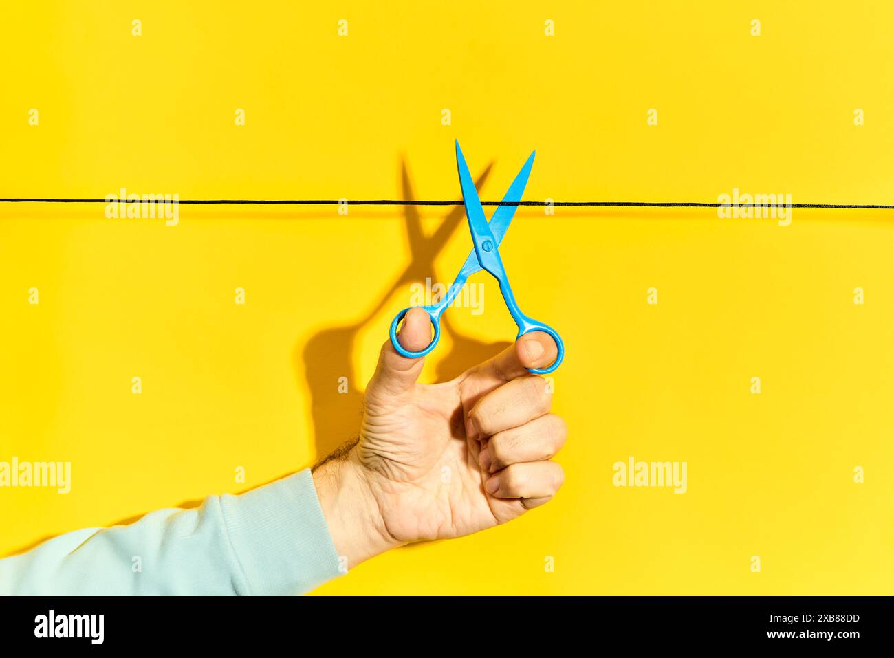 Male hand holding blue scissors and cutting rope on yellow background ...