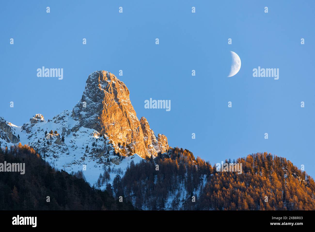 Winter landscape view of the moon above the Pierre Avoi mountain illuminated by the setting sun, shot from Saxon Wallis Stock Photo