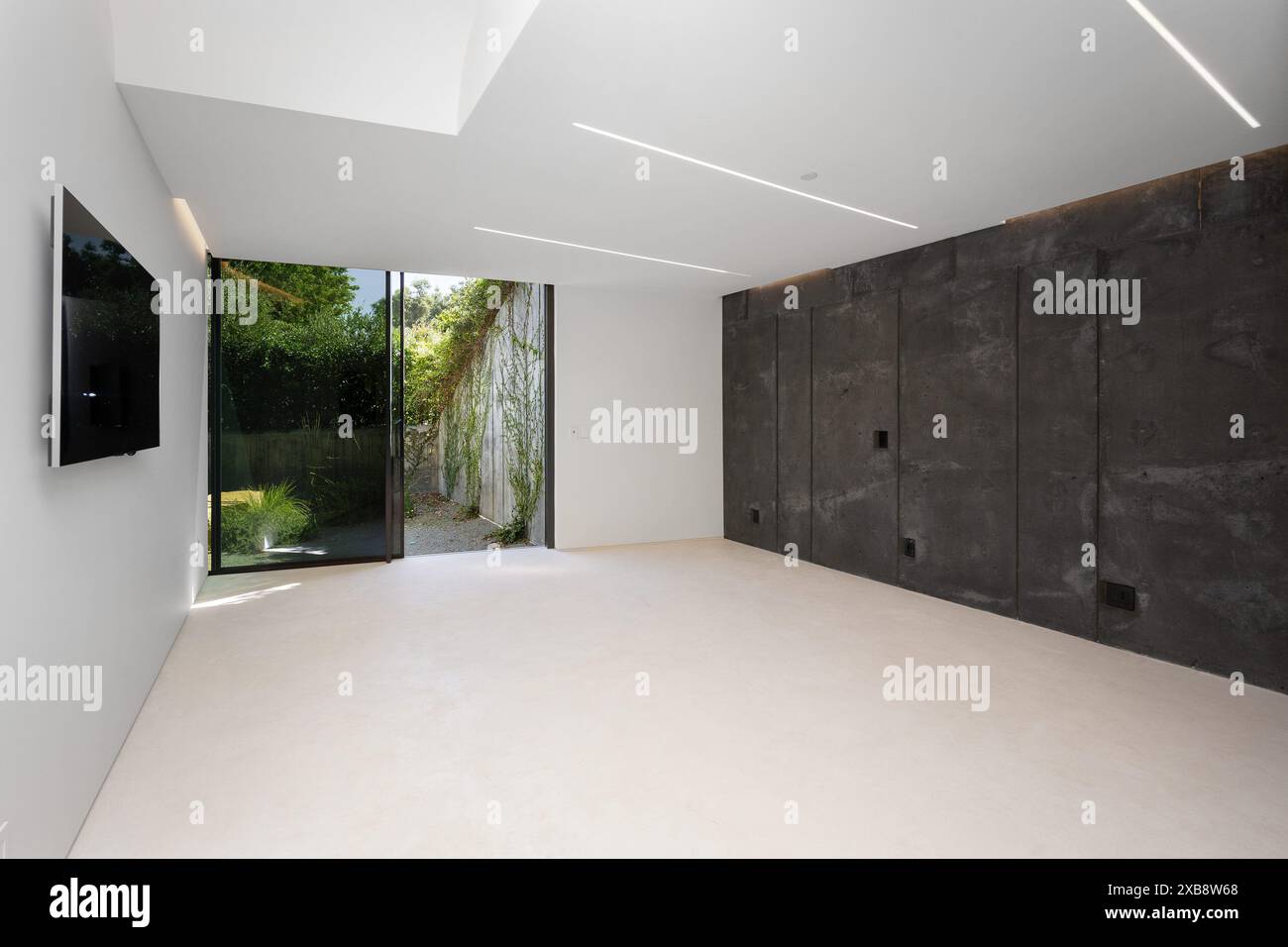 Minimalist room with concrete walls, white floors, and wall-mounted TV Stock Photo