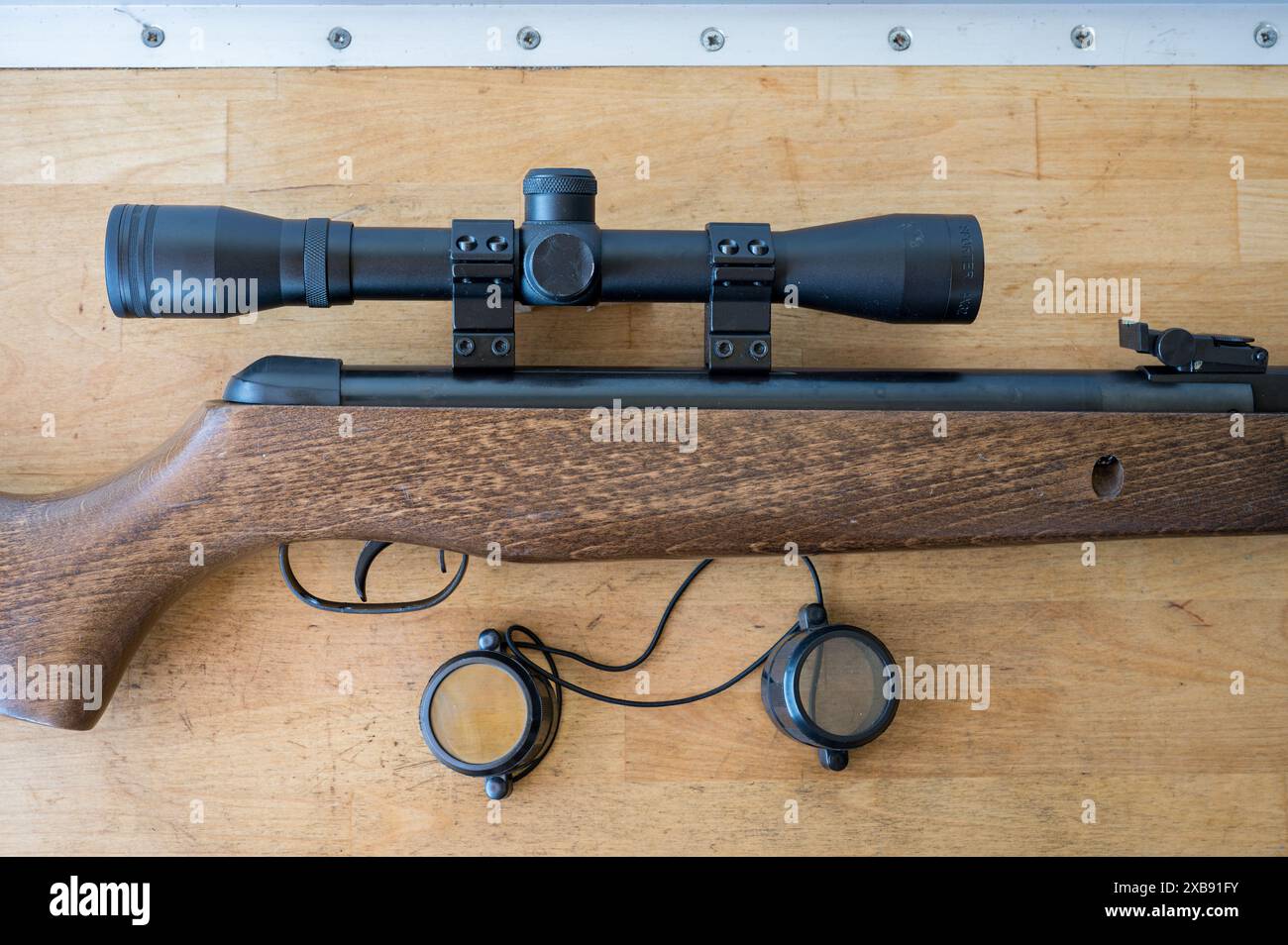 Detail of a light precision air rifle with optical sight on a wooden table. It is a 4.5mm