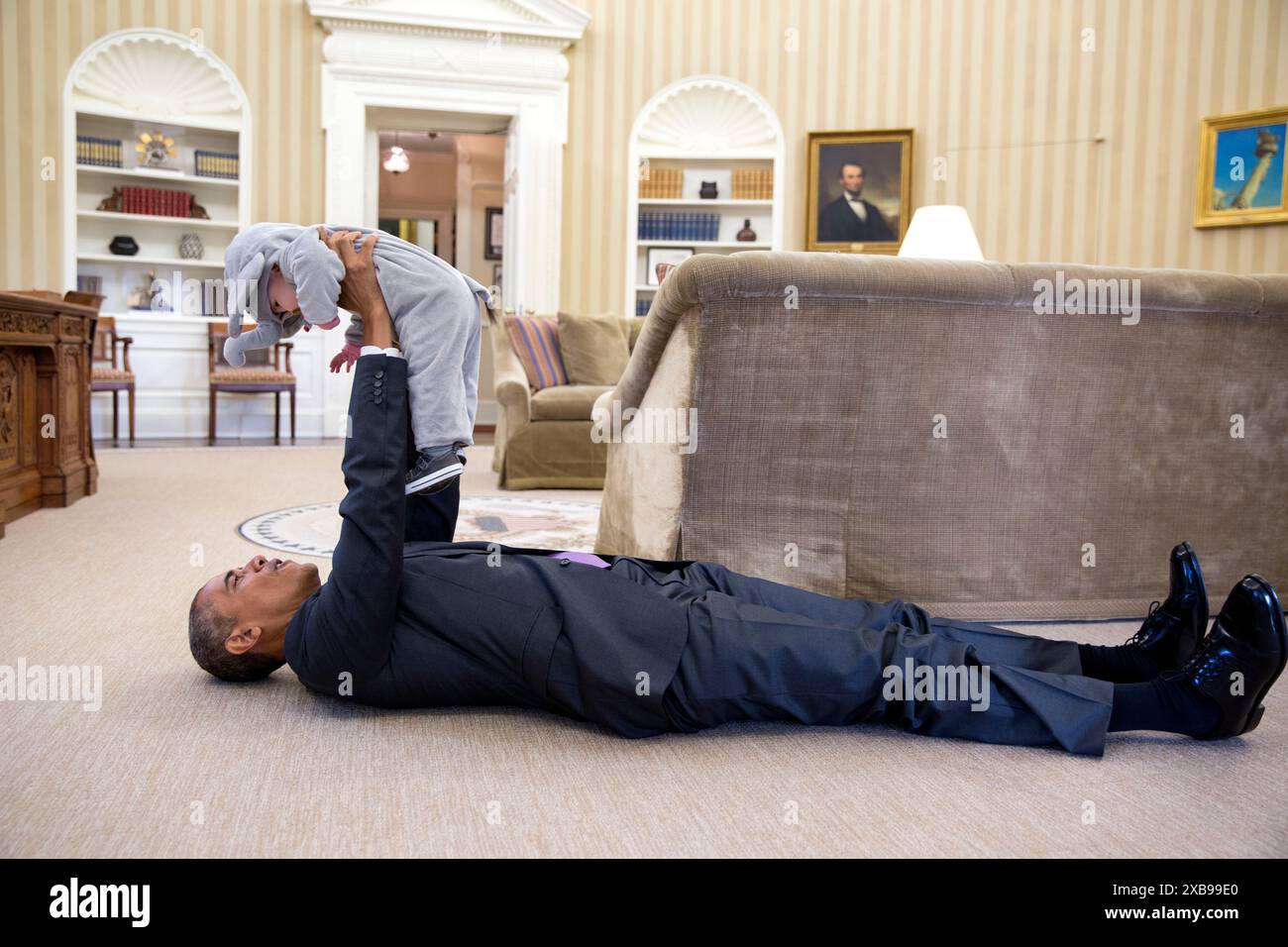 President Barack Obama holds Ella Harper Rhodes, daughter of Ben Rhodes, Deputy National Security Advisor for Strategic Communications, as he lies on the floor in the Oval Office - White House official photographer Stock Photo