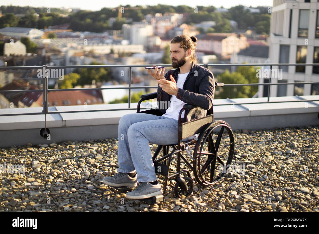Young man using smartphone while sitting in wheelchair on rooftop Stock Photo