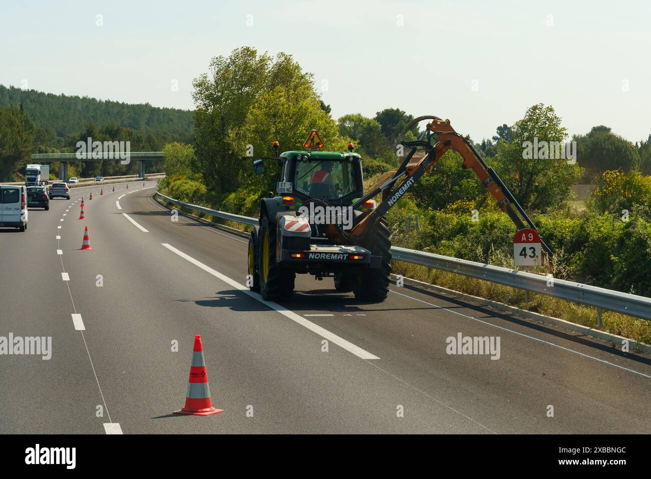Salles-d'Aude, France - May 16, 2023: A maintenance worker operates an excavator on the side of a highway, with traffic cones set up for safety during Stock Photo