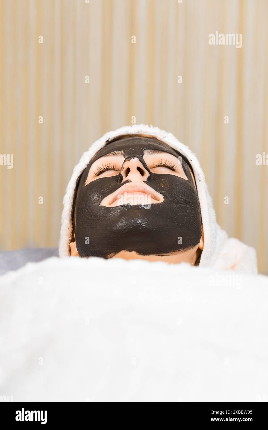 Skin care. A young woman with black cosmetic mask on her face. Woman in charcoal mask on face in spa beauty salon. Stock Photo