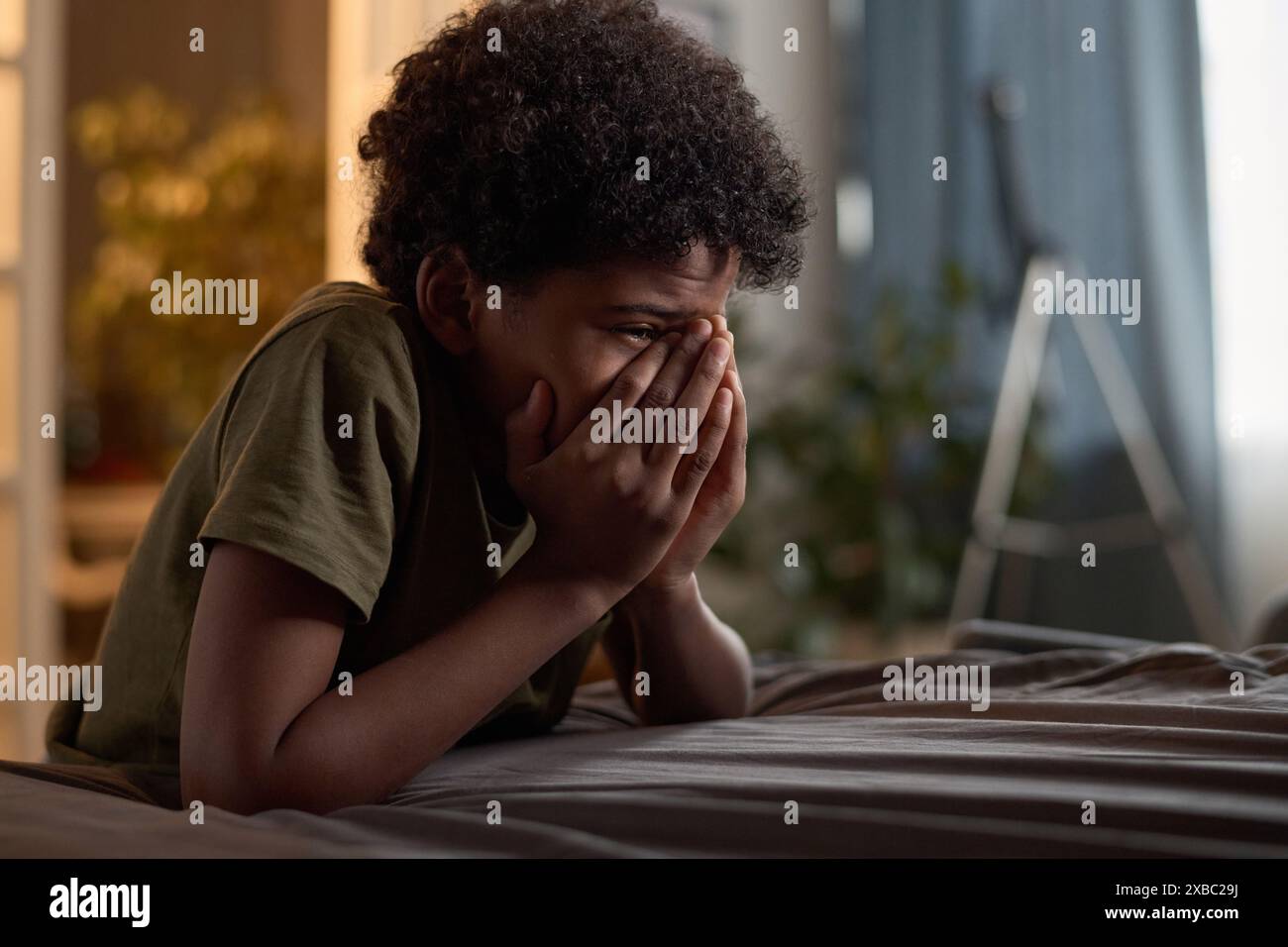 Side view portrait of hysterical young boy crying hiding in his room and covering face copy space Stock Photo