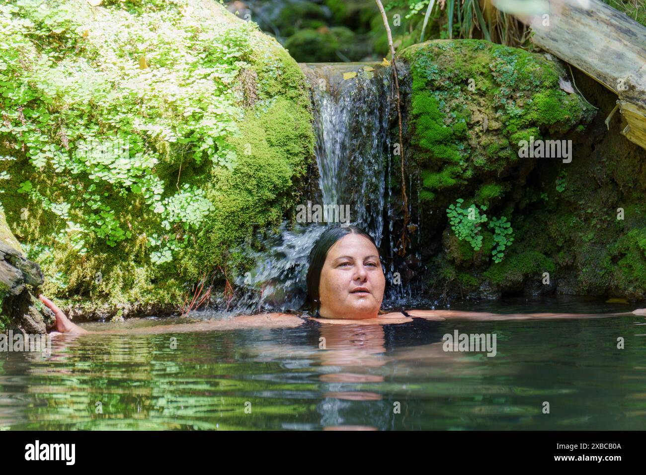 Woman bathing in a crystal-clear river under a moss-covered rock