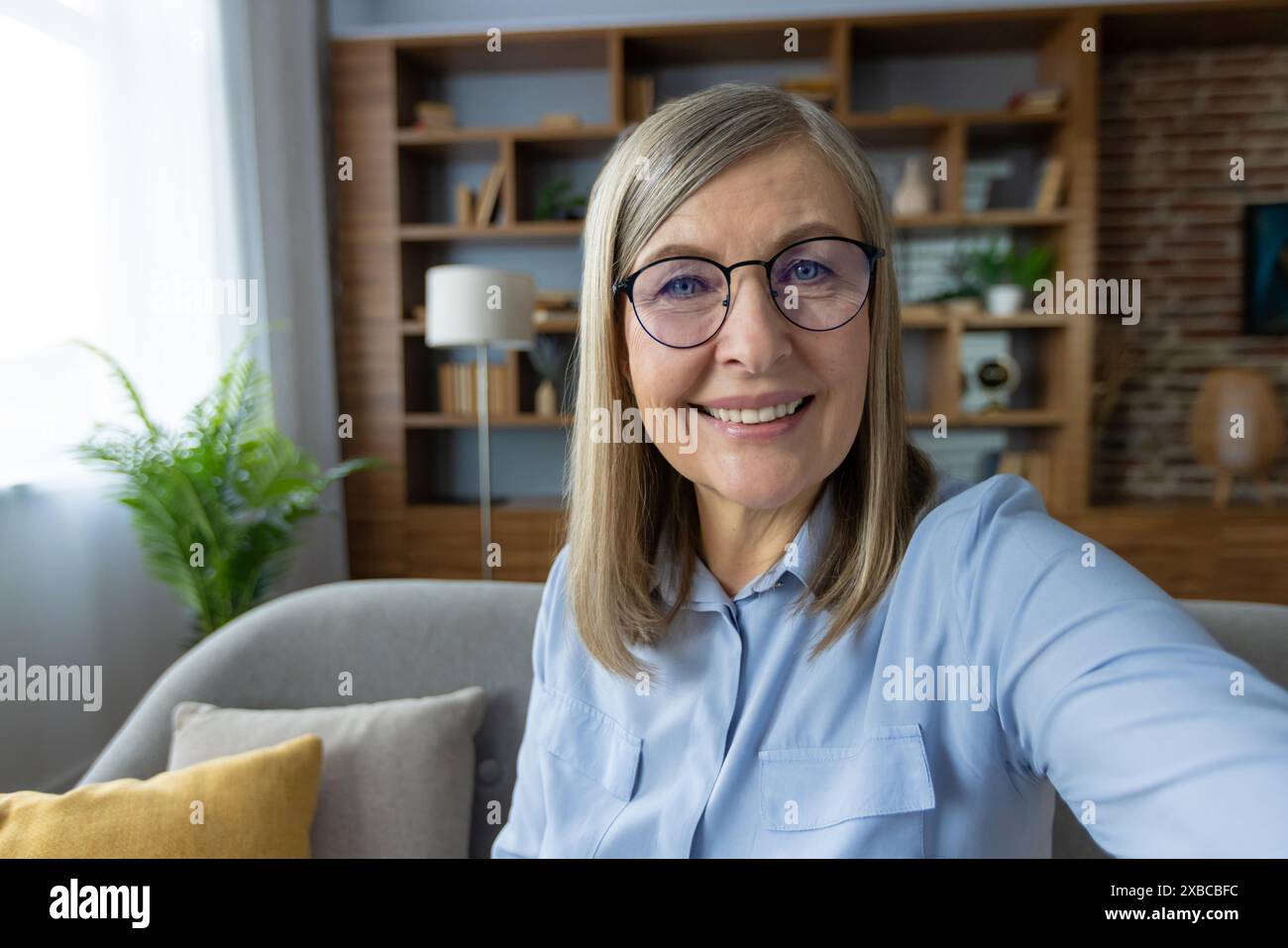 Senior woman with glasses taking a selfie at home in a modern, cozy ...