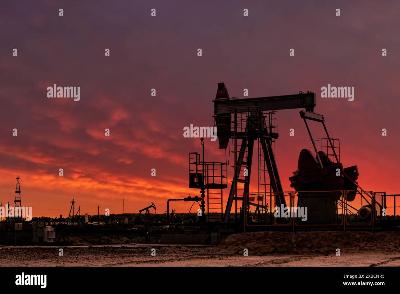 Oil drill rig silhouette and pump jack at sunset background. Oil