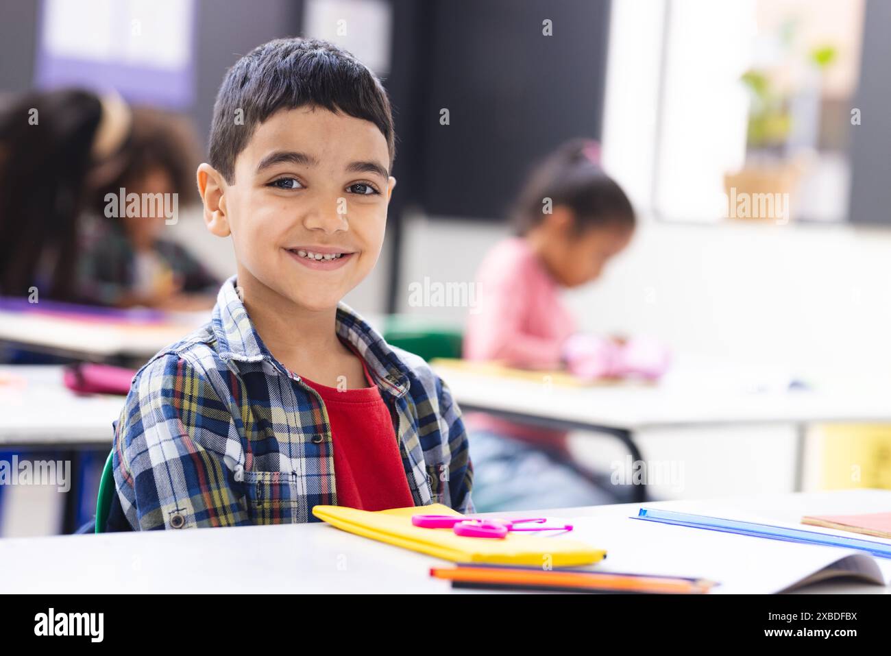 Biracial boy smiling at desk in classroom with school supplies around ...