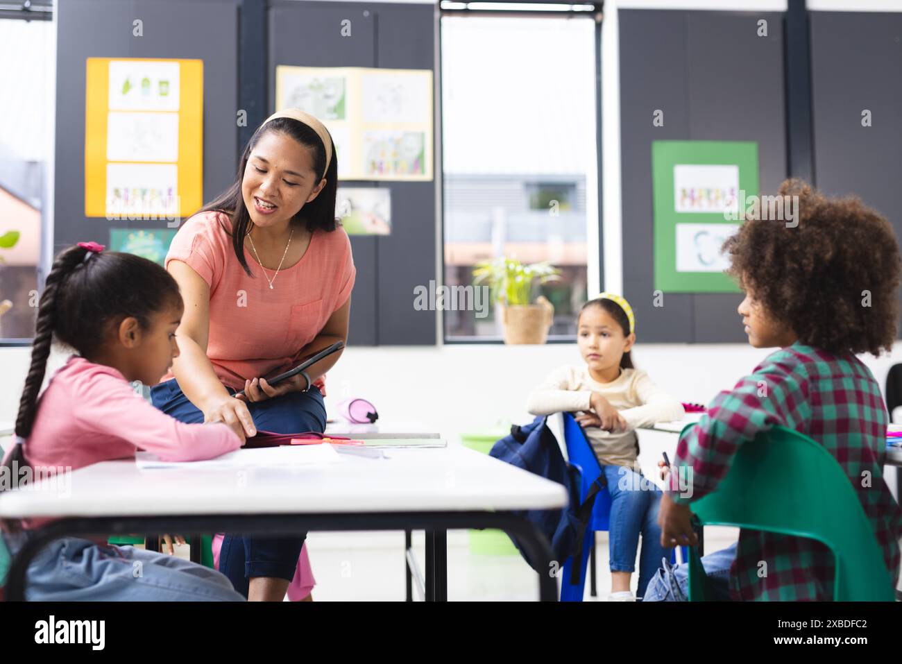 A biracial teacher helping group of biracial students in classroom ...