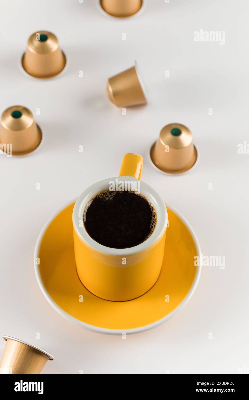 Yellow coffee cup with golden coffee capsules on a white background. Stock Photo