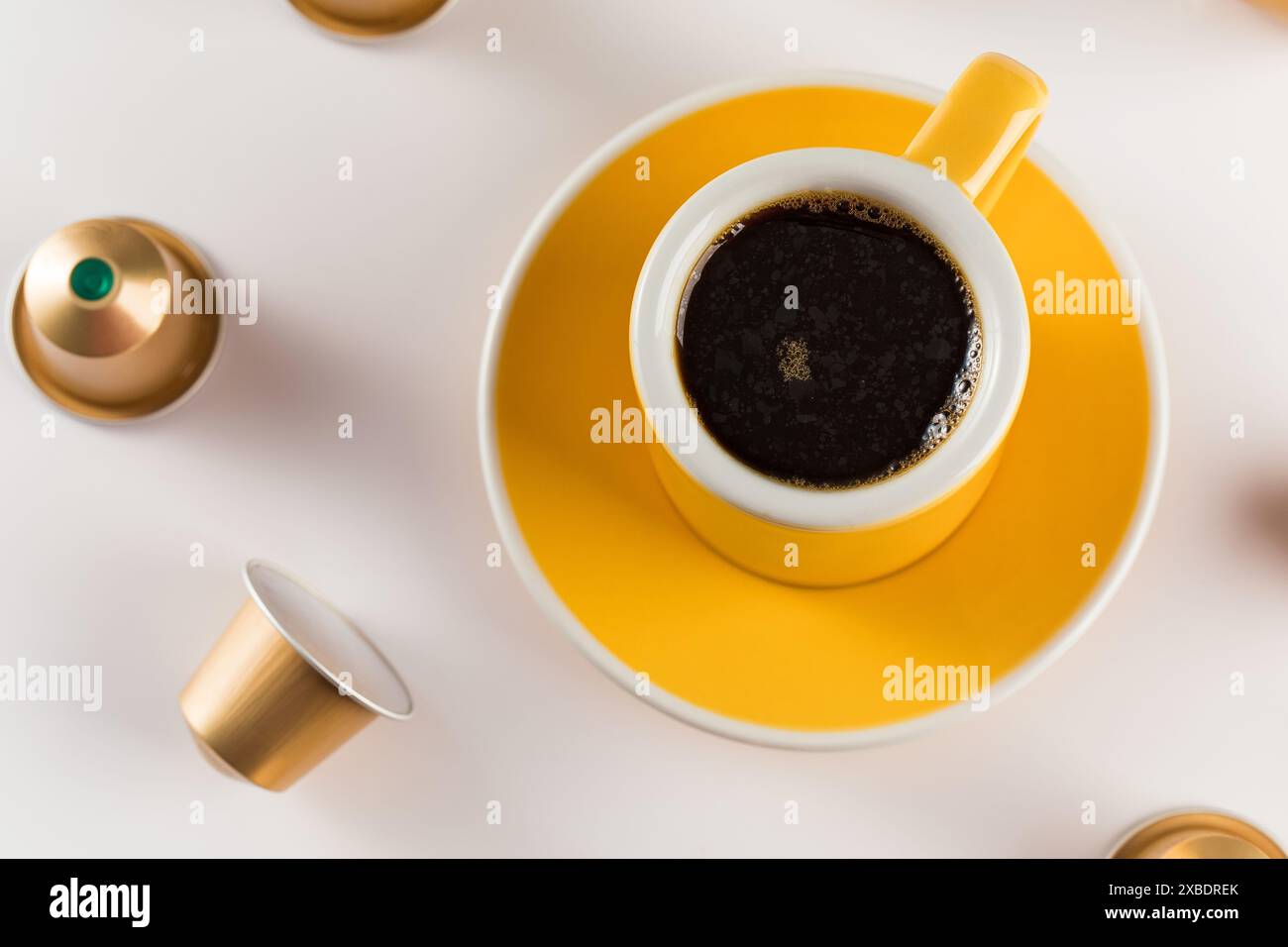 Yellow coffee cup with golden coffee capsules on a white background. Stock Photo