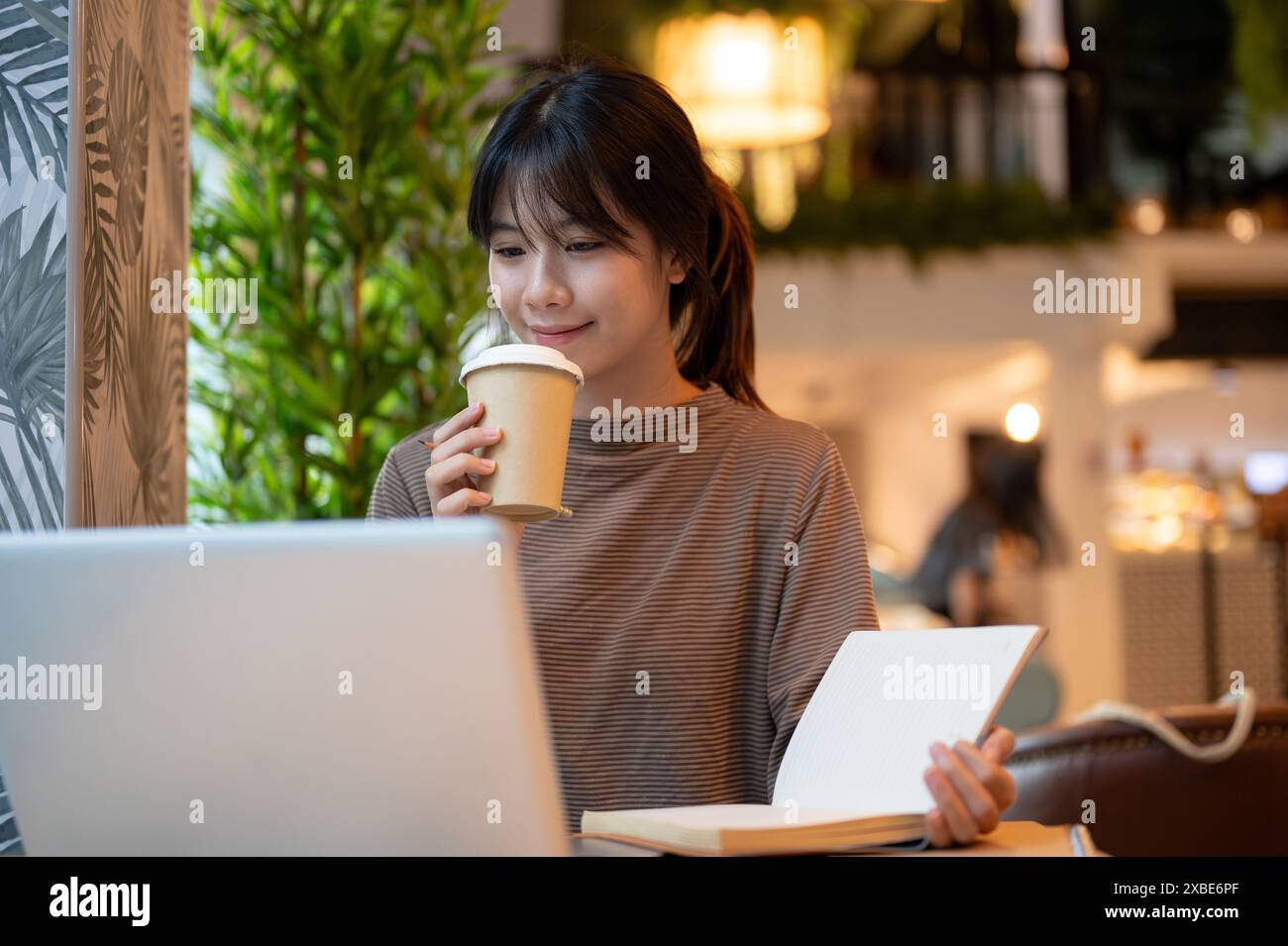 A young attractive Asian woman working remotely in a coffee shop ...