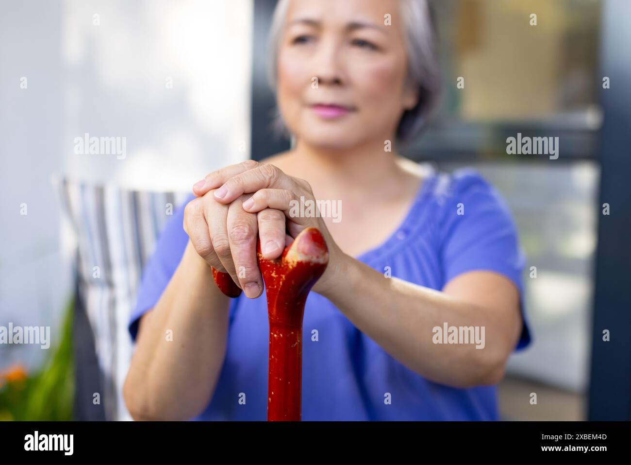 Asian senior woman holding cane with both hands, looking thoughtful, at home Stock Photo