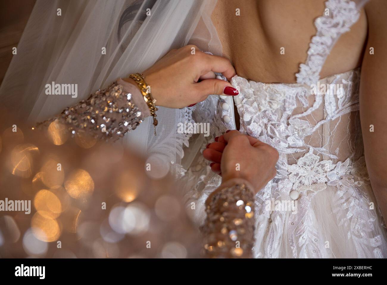 A close-up of a bride's dress being buttoned up by a bridesmaid with sequined sleeves. Stock Photo