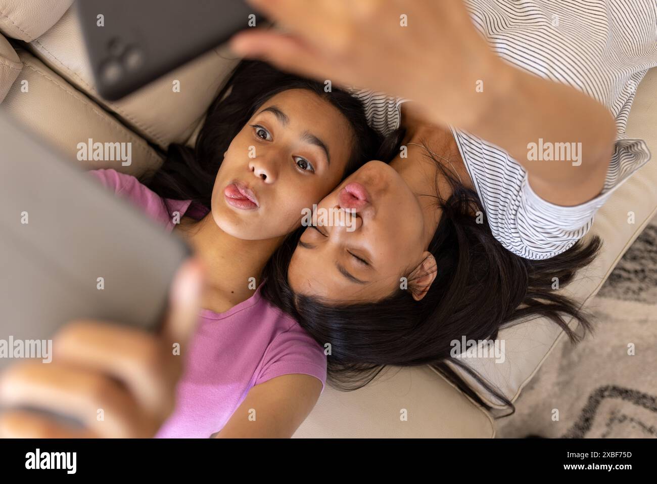 Two young biracial sisters are taking selfie together while lying on a couch, at home Stock Photo