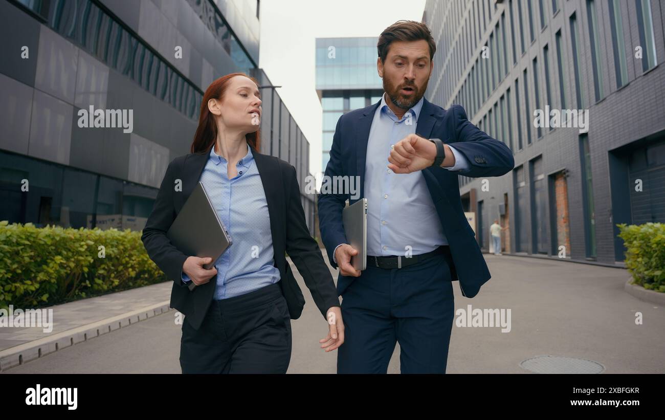 Caucasian businesspeople business colleagues coworkers partners managers businesswoman businessman walking in city talking check time look at writ Stock Photo