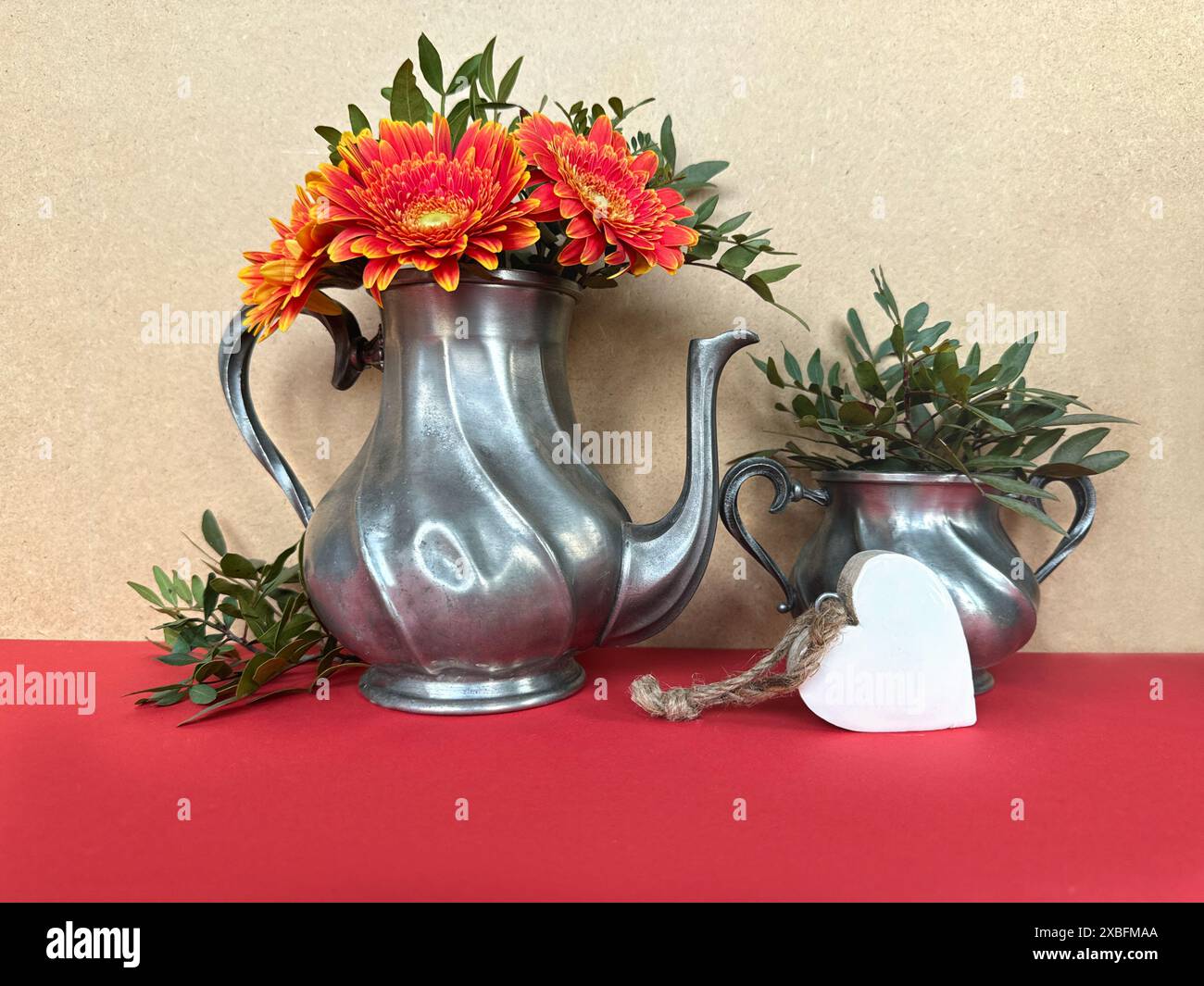 Vintage Metal Teapots with Bright Red Flowers and Greenery on Red Tablecloth Stock Photo