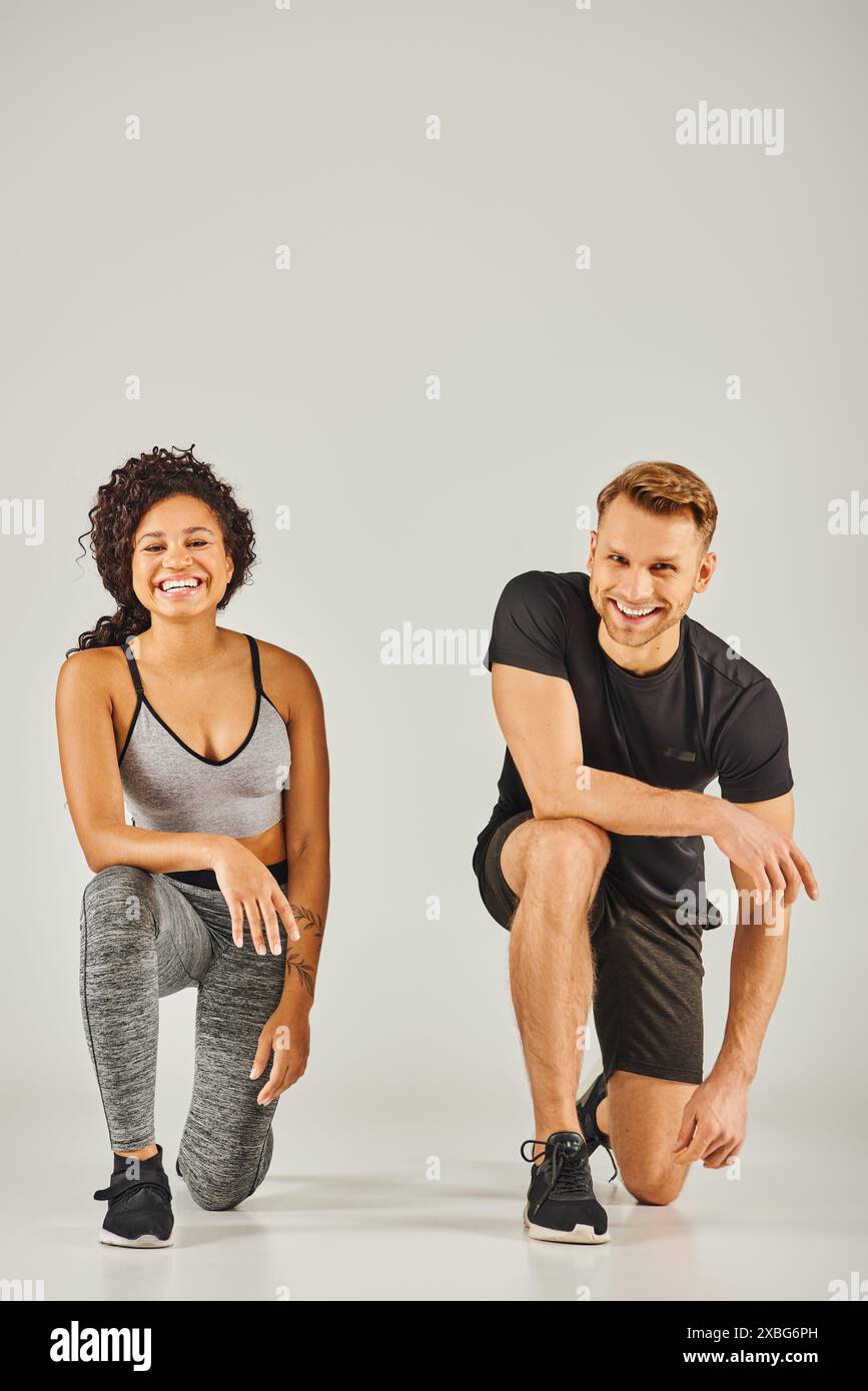 Young interracial sport couple squatting together in active wear on grey background in a studio setting. Stock Photo