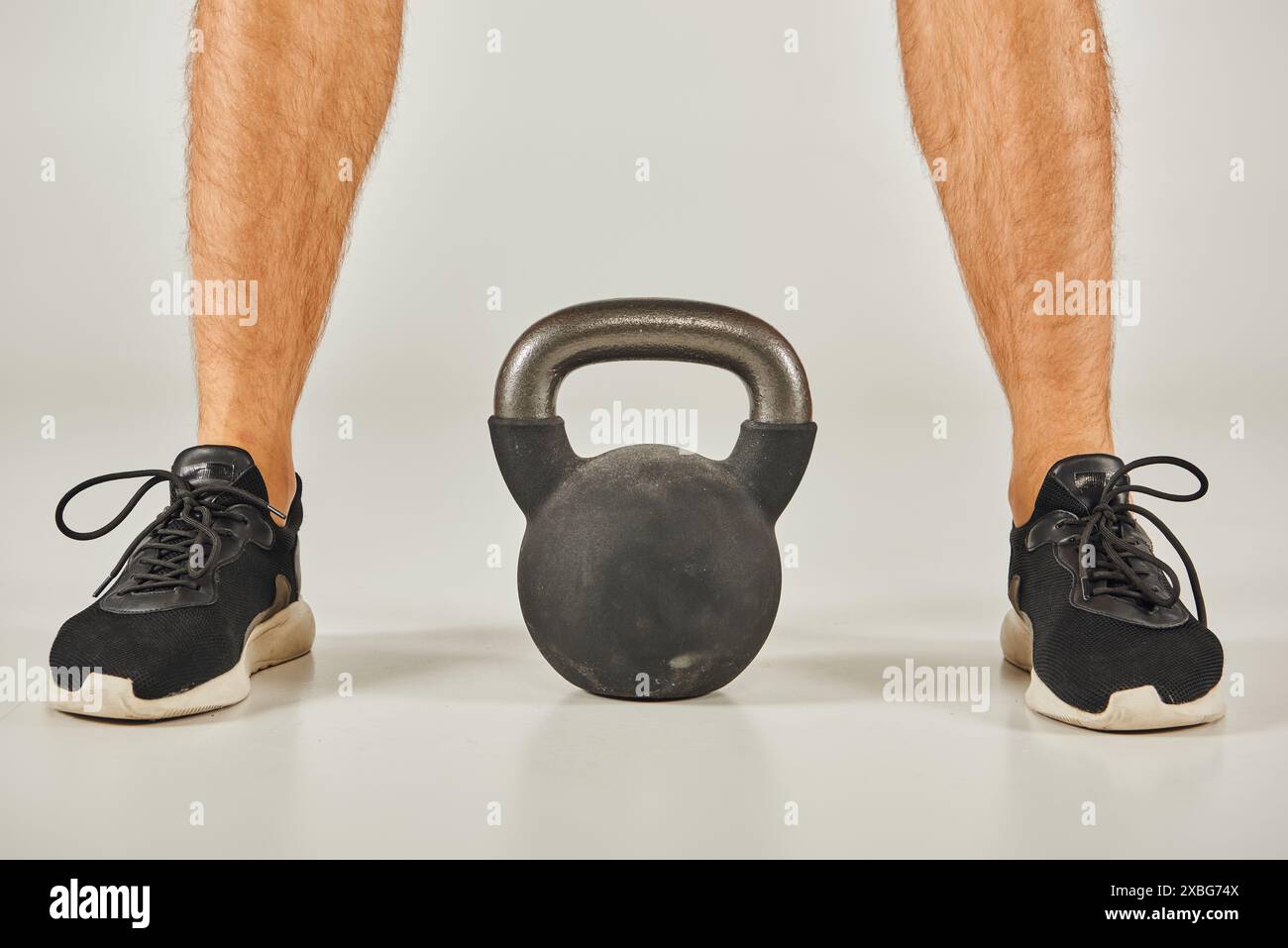 Young sportsman in active wear standing next to a kettlebell in a studio with a grey background. Stock Photo