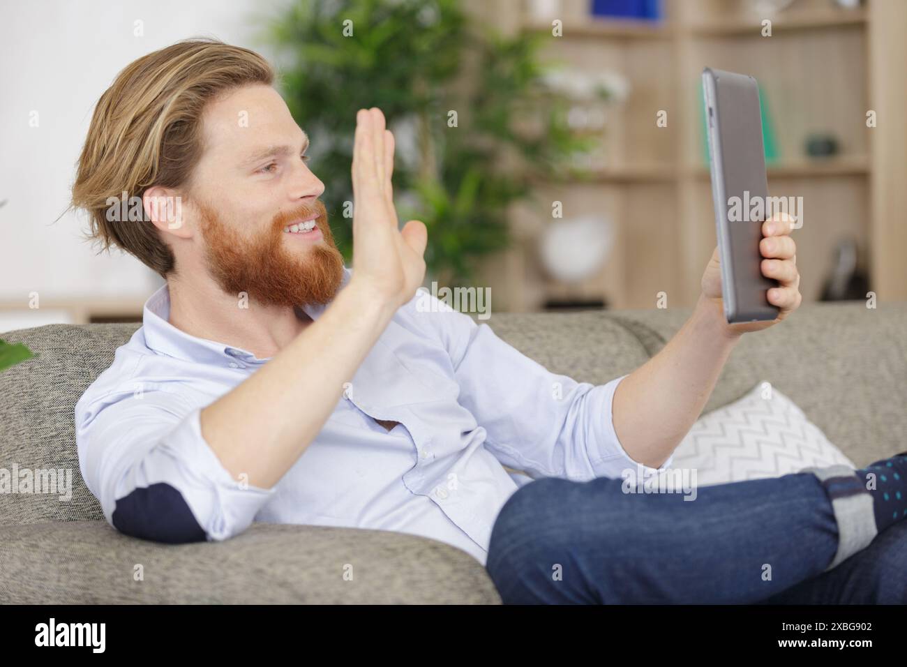 smiling man using tablet for vidn©o chat on his couch Stock Photo