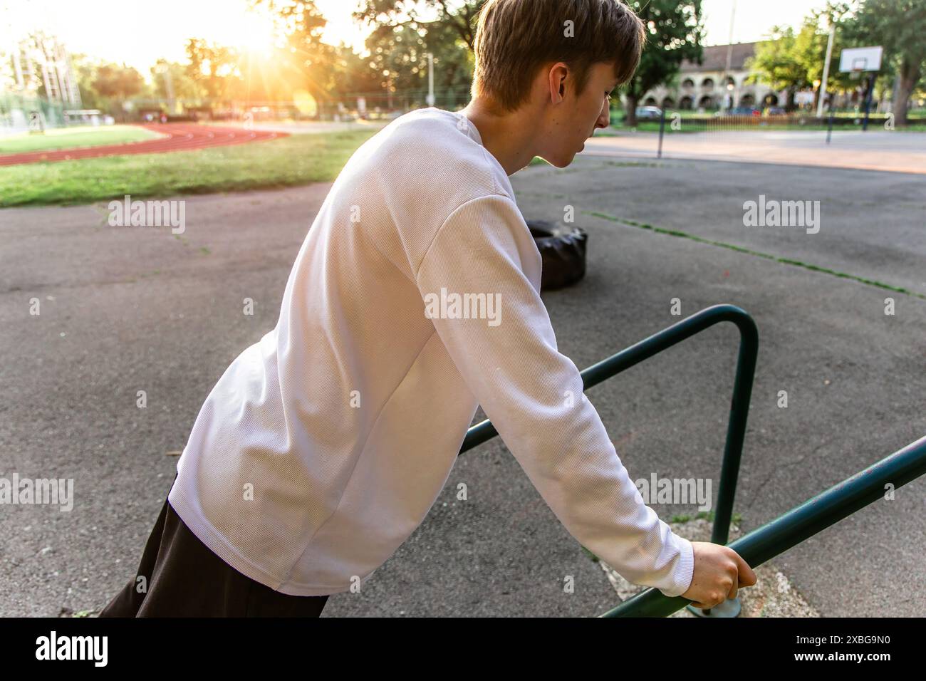 Young Man Doing Dips on a Park Railing at Sunset Stock Photo
