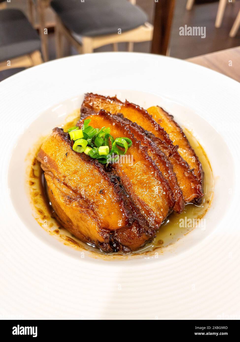 Steamed and braised Pork Belly garnished with green onions, served in a savory sauce, presented on a white plate. Stock Photo
