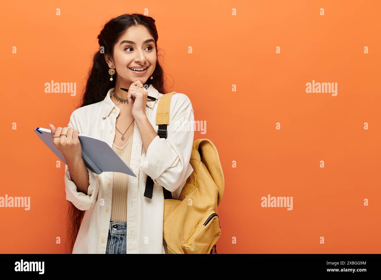 Young indian woman holding a notebook in front of an orange wall Stock ...