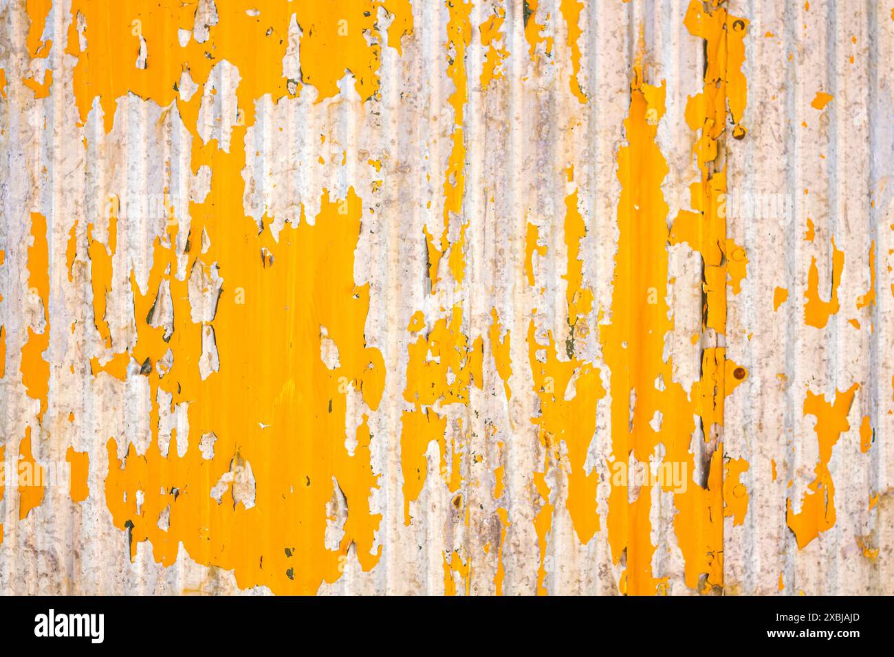 Close up of a weathered corrugated metal surface with peeling yellow paint, revealing rust and wear underneath. Stock Photo