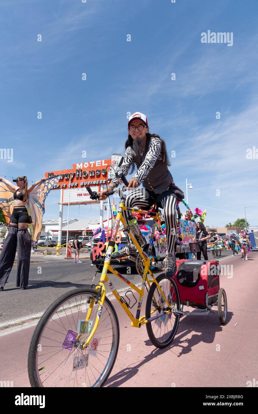 Person in costume rides tall bike pulling cloth covered wagon in Pride