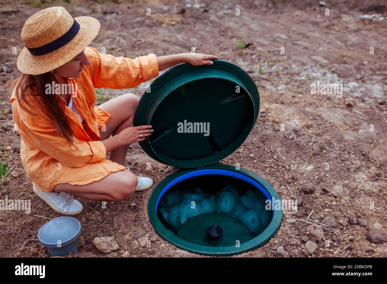 Woman checking autonomous sewage system lifting lid of plastic septic. Biological wastewater sewerage underground tank Stock Photo