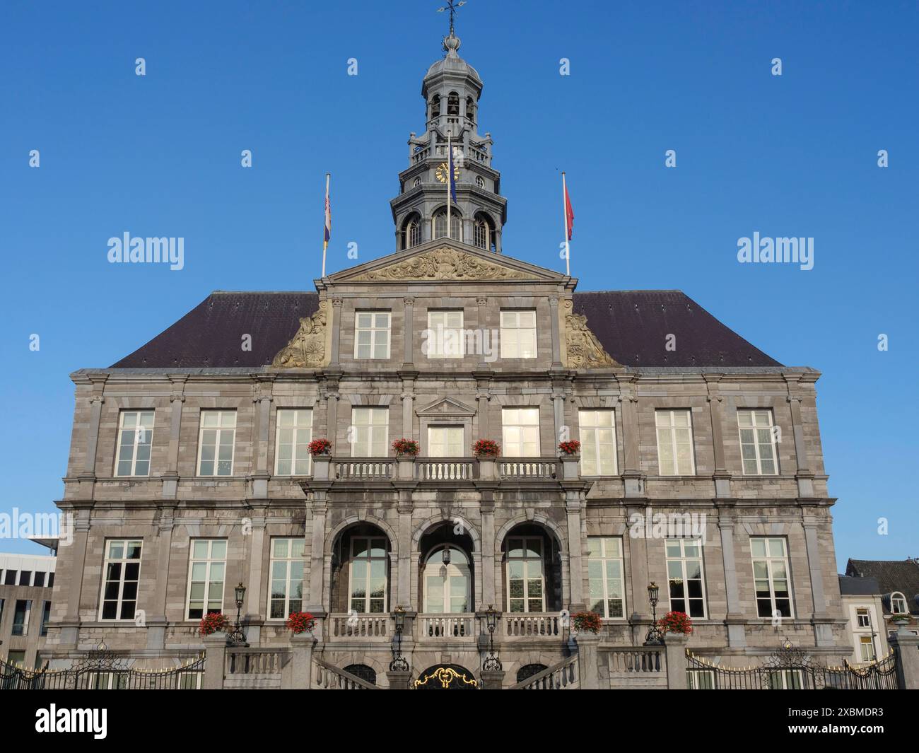 Historic town hall with stone facade and flags against a clear blue sky ...