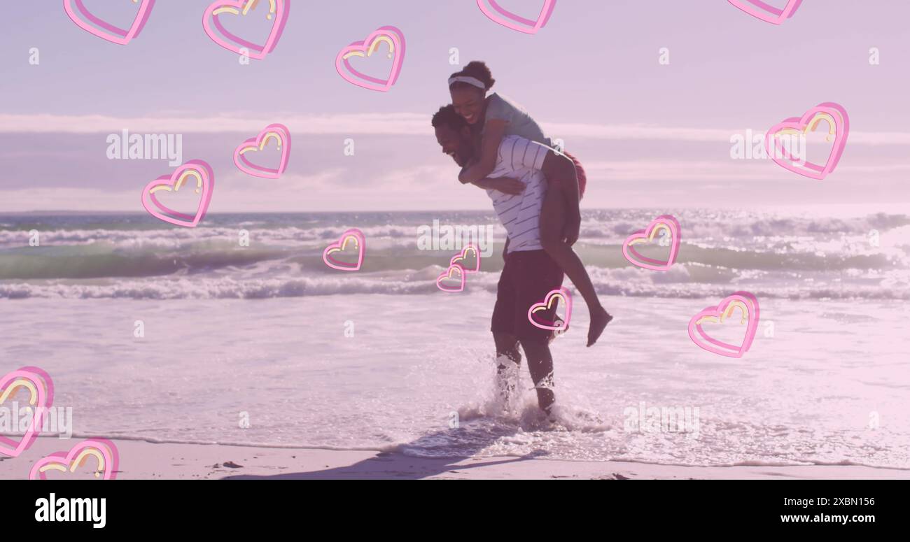 Image of pink hearts over happy african american couple piggybacking on beach Stock Photo