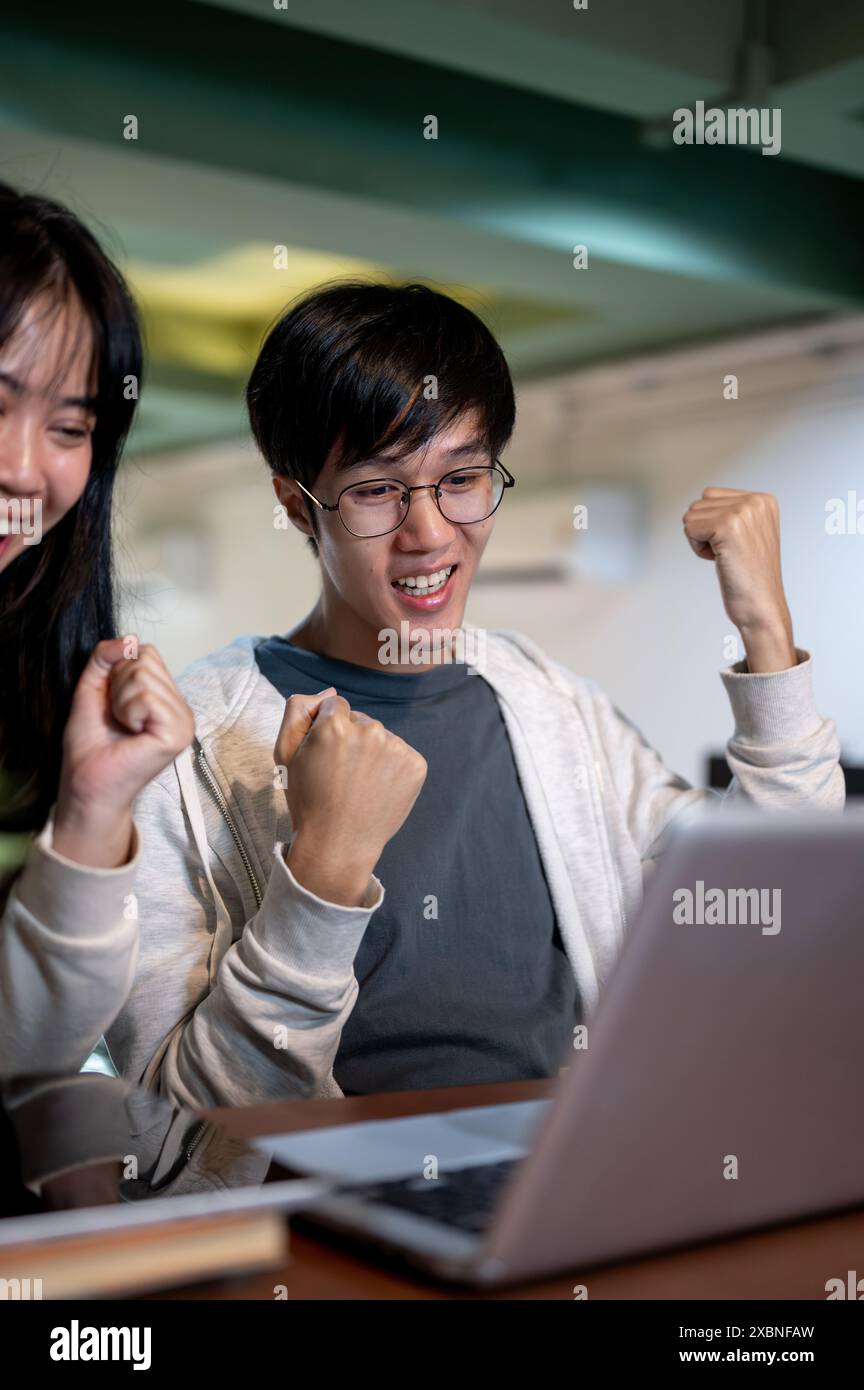 A young, cheerful Asian male college student is looking at a laptop ...